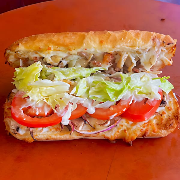 A Detroit Pizza sub sandwich with melted cheese, lettuce, tomatoes, and sauce on an orange surface.
