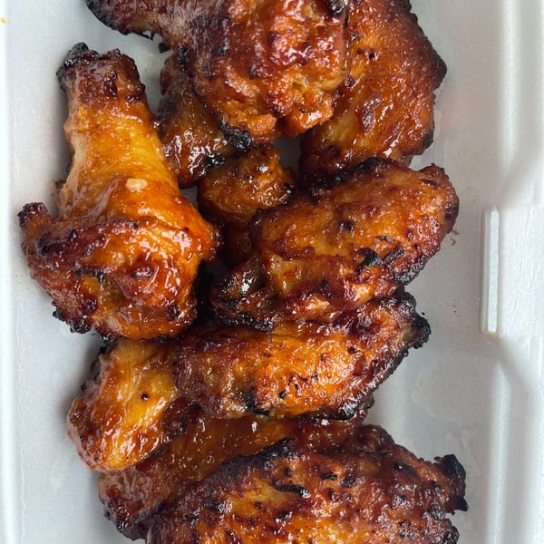 Close-up of several glossy, golden-brown chicken wings with charred edges in a white container.