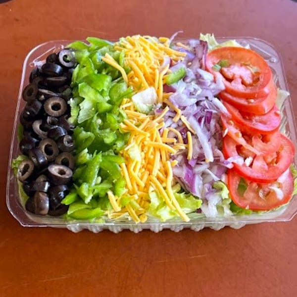 A clear plastic container filled with a fresh salad, featuring olives, green peppers, cheese, red onion, and tomatoes.
