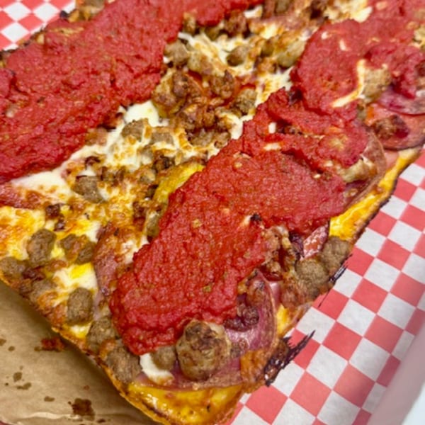 Close-up of a Detroit-style pizza with thick red sauce stripes, melted cheese, and sausage crumbles.