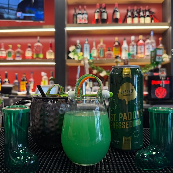 St. Patrick's Day themed drinks, including a green cocktail with a rainbow candy garnish, at a bar.