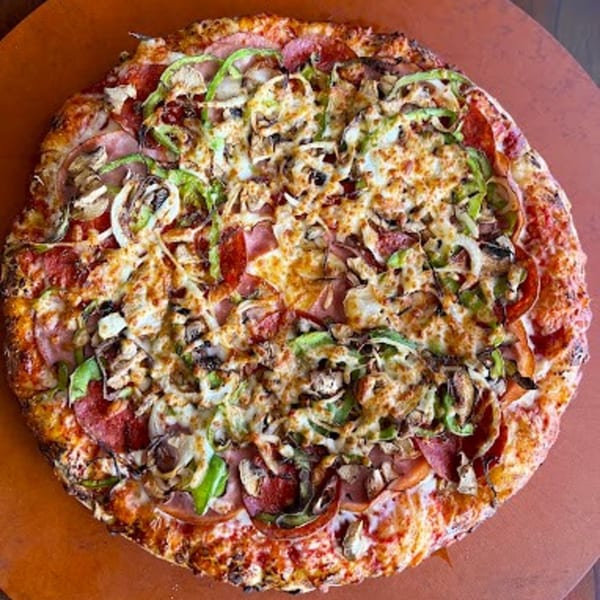 A Detroit-style pizza with pepperoni, ham, green peppers, onions, and mushrooms on a brown surface.