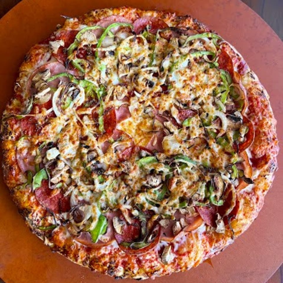 A Detroit-style pizza with pepperoni, ham, green peppers, onions, and mushrooms on a brown surface.