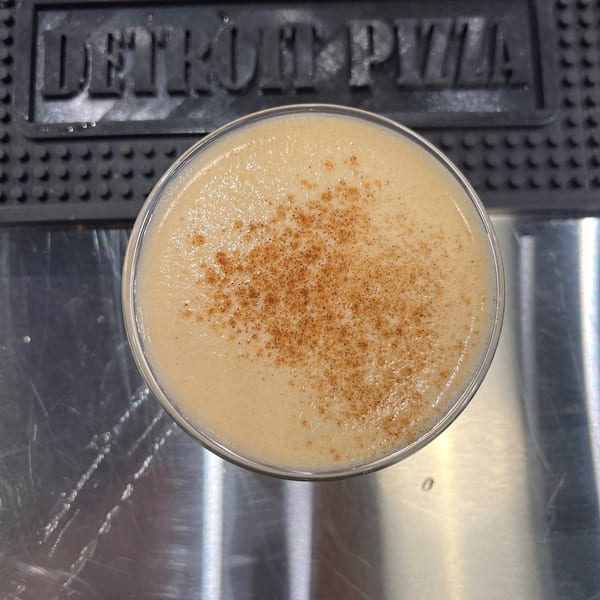 Creamy cocktail with cinnamon dusting on a bar mat with "Detroit Pizza" logo.
