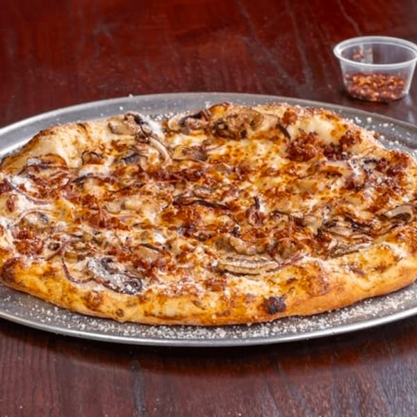 Detroit Pizza's mushroom and onion pizza on a metal tray with a side of red pepper flakes.