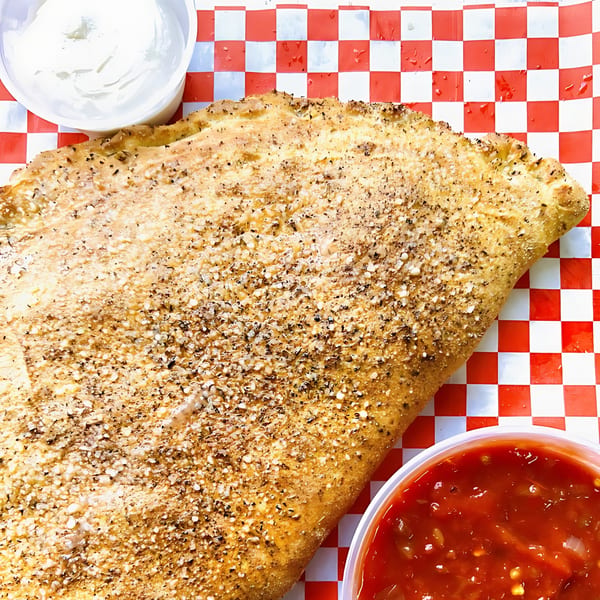 A large, golden-brown calzone sprinkled with herbs and cheese, served with marinara and white dipping sauces.