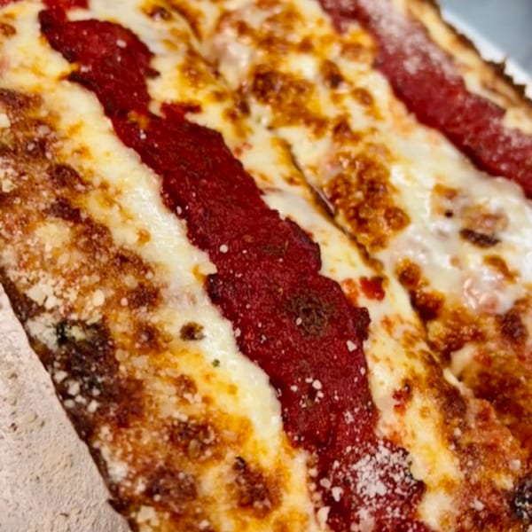 Close-up of a Detroit-style pizza slice with thick red sauce stripes and melted cheese.