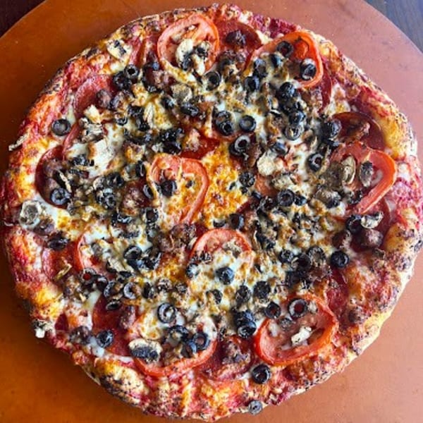 Detroit Pizza with pepperoni, sliced tomatoes, black olives, and mushrooms on a brown surface.