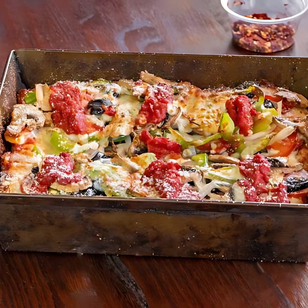 A Detroit-style pizza in a rectangular pan, topped with red sauce, cheese, and vegetables.